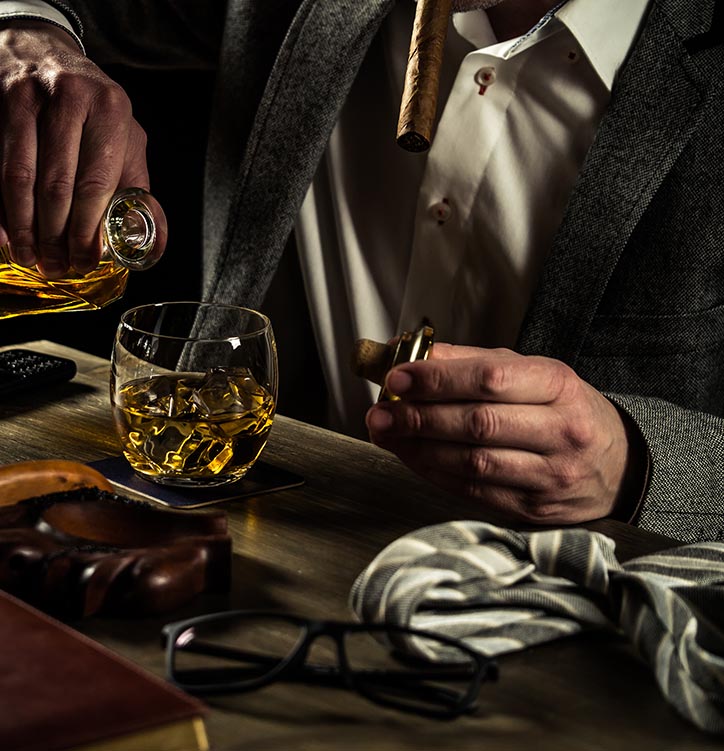 A glass of fine aged bourbon on a bar counter next to a premium cigar at Chairman's Club in Farmington, MI.