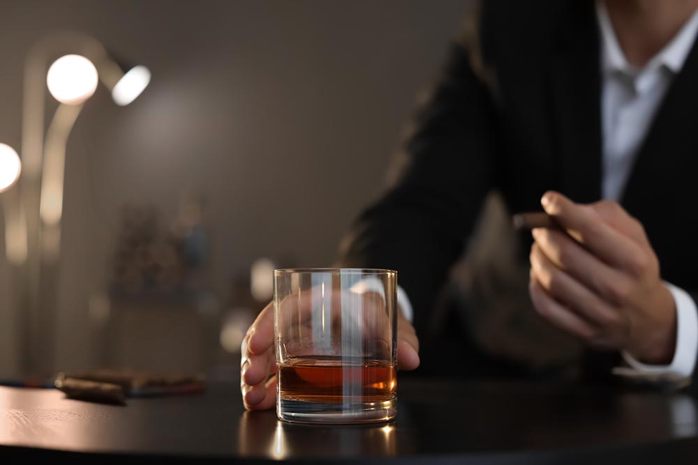 A glass of fine aged bourbon on a bar counter next to a premium cigar at Chairman's Club in Livonia, MI.
