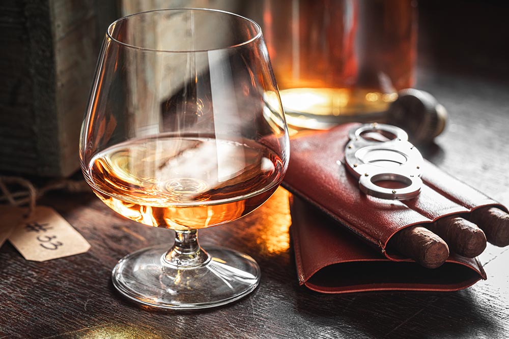 A glass of fine aged bourbon on a bar counter next to a premium cigar at Chairman's Club in Northville, MI.